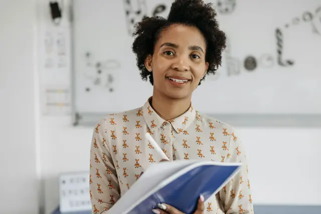Docent met notitieboek die glimlachend voor de klas staat